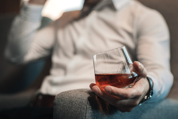 Tired businessman holding glass of whisky sitting in armchair