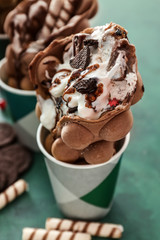 Delicious bubble waffles with ice cream in cups on color table