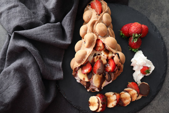 Delicious bubble waffle with ice cream and fruits on slate plate