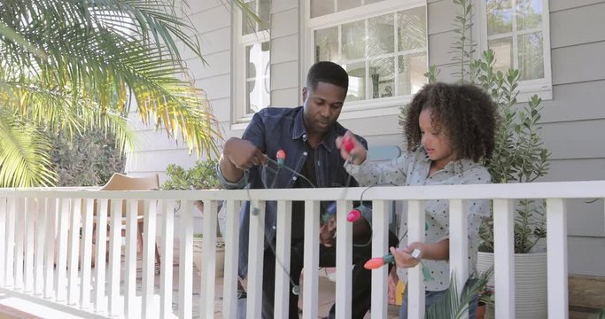 African American father and daughter hanging christmas lights outdoors