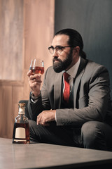 Bearded stylish man wearing red tie drinking glass of whisky
