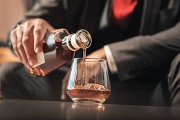 Businessman sitting on sofa and pouring cognac into glass