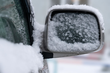 White snow poured on side mirror on the car in the winter.