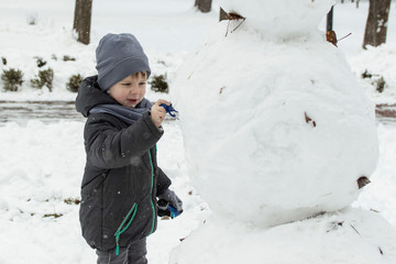 A little boy of 5-7 years old is playing outside in the snow in a park in winter.