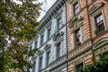 Fototapeta na wymiar Architectural elements of old residential building in downtown Prague, Czech Republic, green blurred tree branches and blossoming red and pink flowers on balcony with open window