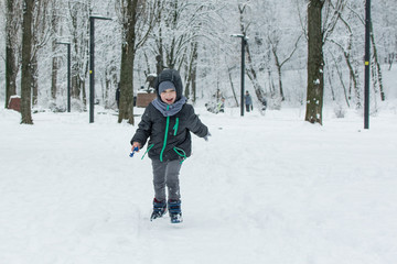 Fototapeta na wymiar A little boy runs through the snow in the park.