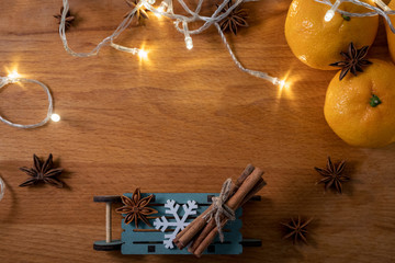 Orange mandarins, cinnamon sticks, anise stars and wooden decorative sled on the wooden background with garlands