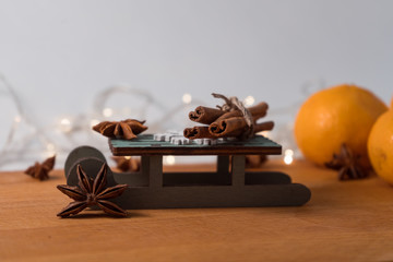 Orange mandarins, cinnamon sticks, anise stars and wooden decorative sled on the wooden background with garlands