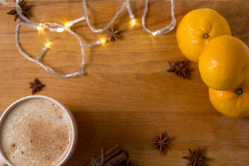 Cup of coffee  with orange mandarins and cinnamon sticks and anise stars sticks on the wooden table with garland