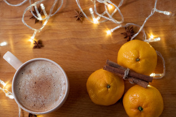 Cup of coffee  with orange mandarins and cinnamon sticks on the wooden table with garland