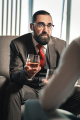 Bearded dark-haired man wearing red tie holding glass of whisky