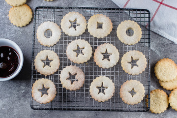 Holiday Sweet Food. Process making of cookies. Christmas Linzer cookies with red berry jam on gray concrete table background. Top view, flat lay