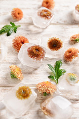 Beautiful flowers frozen in ice cubes on light wooden  background