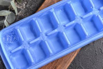 Tray with ice cubes on wooden board