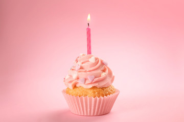 Tasty birthday cupcake with burning candle on color background
