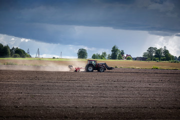 Agricultural background. Tractor pulling plow, throwing dust in air. Combine harvester at wheat field. Heavy machinery during cultivation, working on fields. Dramatic sky, sun rays, rain, storm clouds