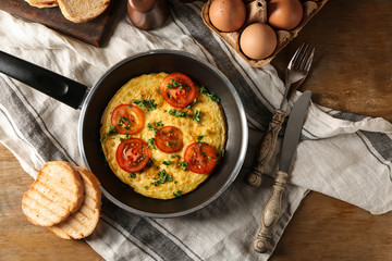 Frying pan with tasty omelet on wooden table