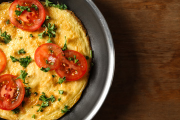 Frying pan with tasty omelet on wooden table