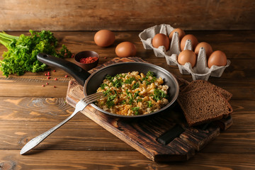 Frying pan with tasty omelet and bread on wooden table