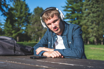 Concerned teenager listening to music with his headphones while sitting alone at a picnic table.