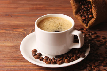 Cup of aromatic coffee and coffee beans on a wooden background.