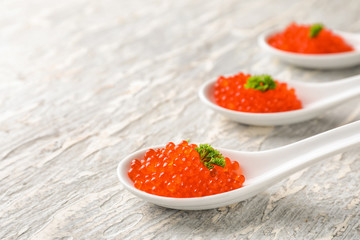 Spoons with delicious red caviar on light table