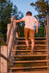 Young man is walking up stairs in nature park next to beach during bright, warm sunset. Romantic evening in nature. Concept of healthy and active lifestyle, recreation and relaxing holidays