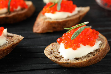 Delicious sandwiches with red caviar on wooden board, closeup