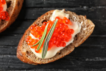 Delicious sandwich with red caviar on wooden board, closeup