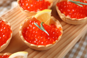 Delicious canapes with red caviar on wooden board, closeup
