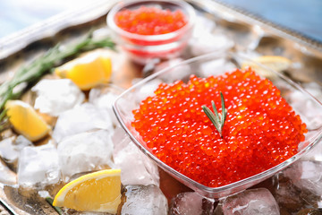 Bowl with delicious red caviar and ice cubes on metal tray, closeup