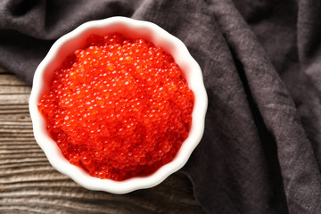 Bowl with delicious red caviar on wooden table