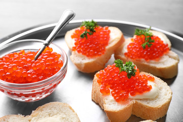 Bowl with delicious red caviar and sandwiches on metal tray, closeup