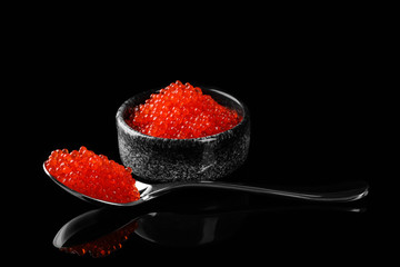 Bowl and spoon with delicious red caviar on dark background