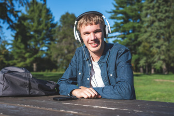 Happy teenager sitting at a picnic table in a park while listening to music.