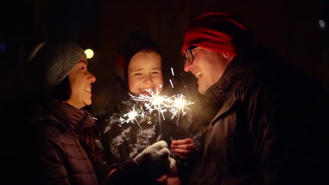 cheerful family celebrating new year's eve on the street in the cold. burning candles sparkle in your hands