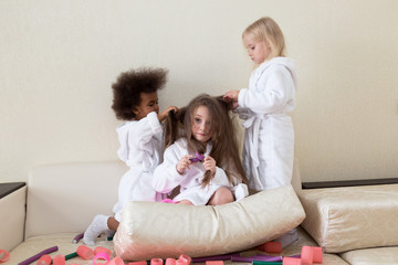 Little girls play with hair curlers and hairpins. Girls girlfriends in white coats braid curlers...