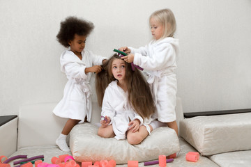 Little girls play with hair curlers and hairpins. Girls girlfriends in white coats braid curlers...
