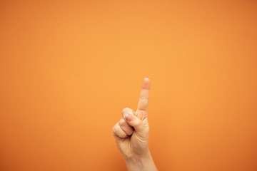 gesture, female index finger shows in top isolated on orange background