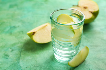 Glass of fresh water with cut apple on color table