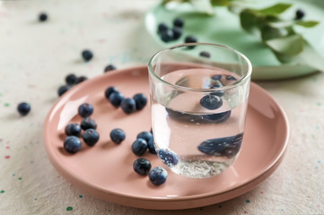 Glass of fresh water with blueberries on plate