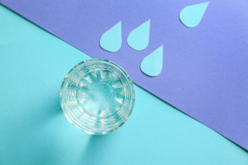 Glass of fresh water with paper drops on color table