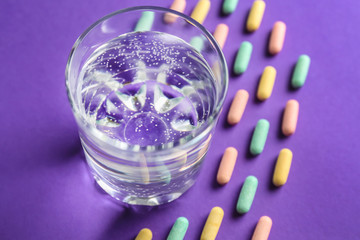 Glass of fresh water with pills on color table