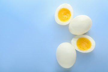 Whole and cut boiled eggs on color background