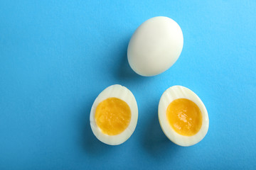 Whole and cut boiled eggs on color background