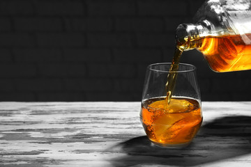 Pouring of whiskey from bottle into glass on wooden table