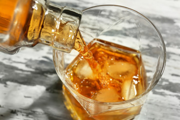 Pouring of whiskey from bottle into glass on wooden table, closeup