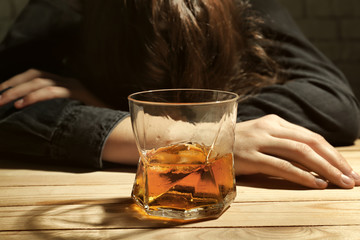 Glass of whiskey on wooden table and unconscious drunk woman in bar