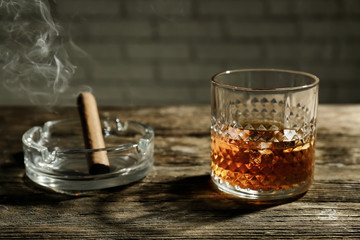 Glass of whiskey with ashtray and cigar on wooden table