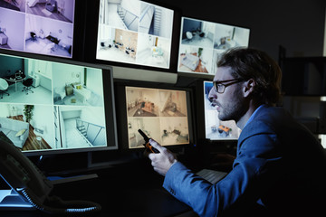 Security guard monitoring modern CCTV cameras in surveillance room